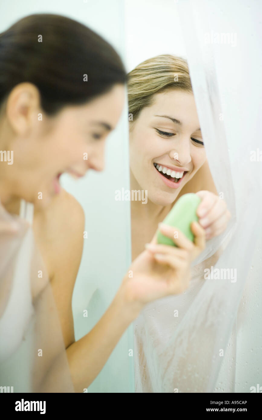 Two young women in showers, one handing bar of soap to the second Stock Photo