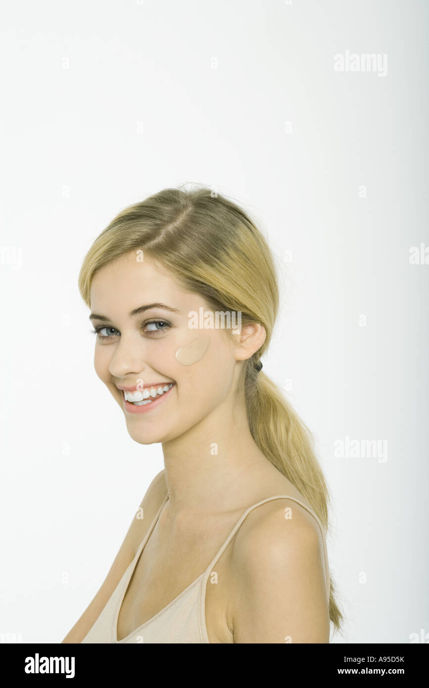 Teenage girl with dollop of foundation on cheek, smiling at camera Stock Photo
