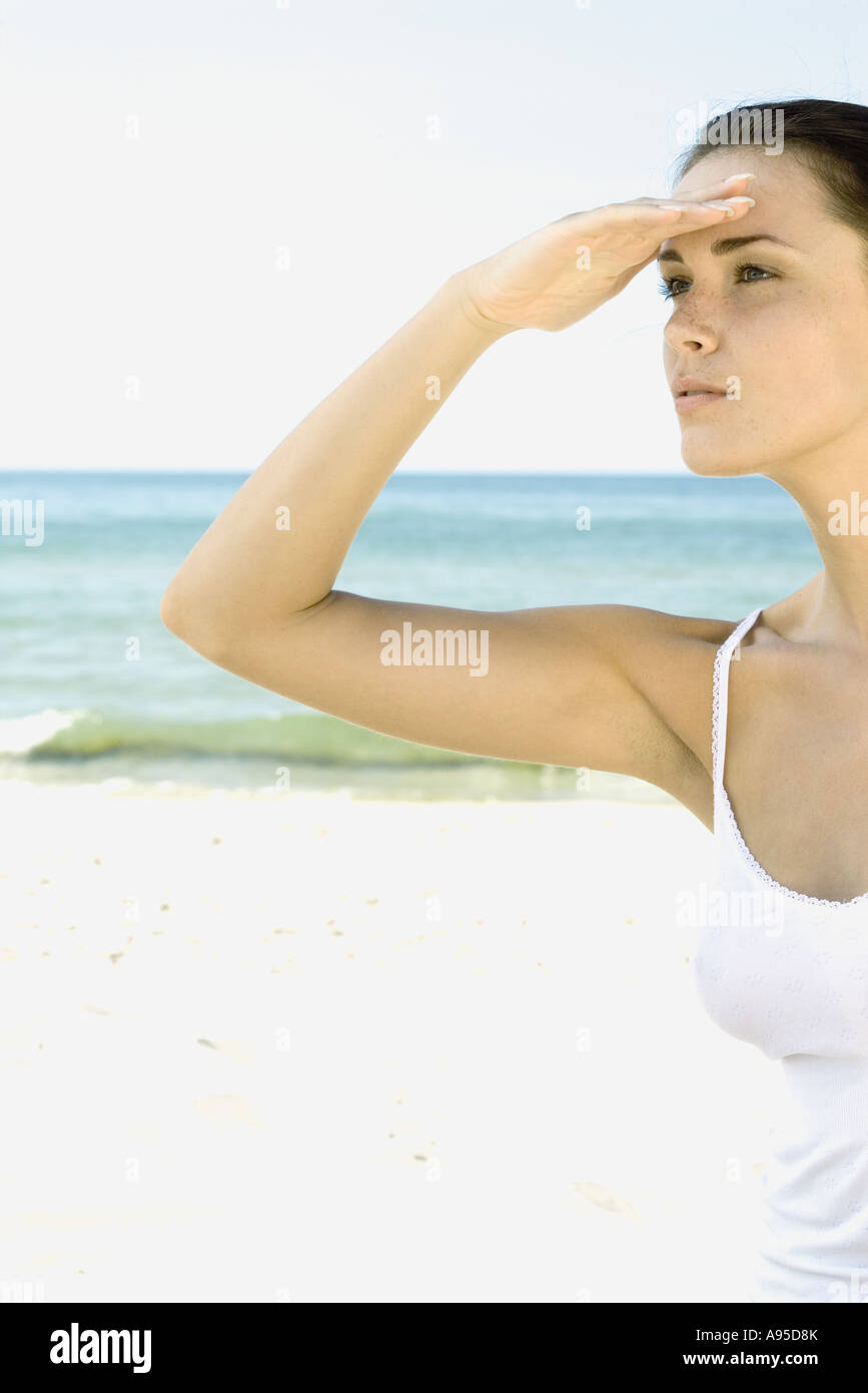 Woman shading eyes, looking away beach in background Stock Photo