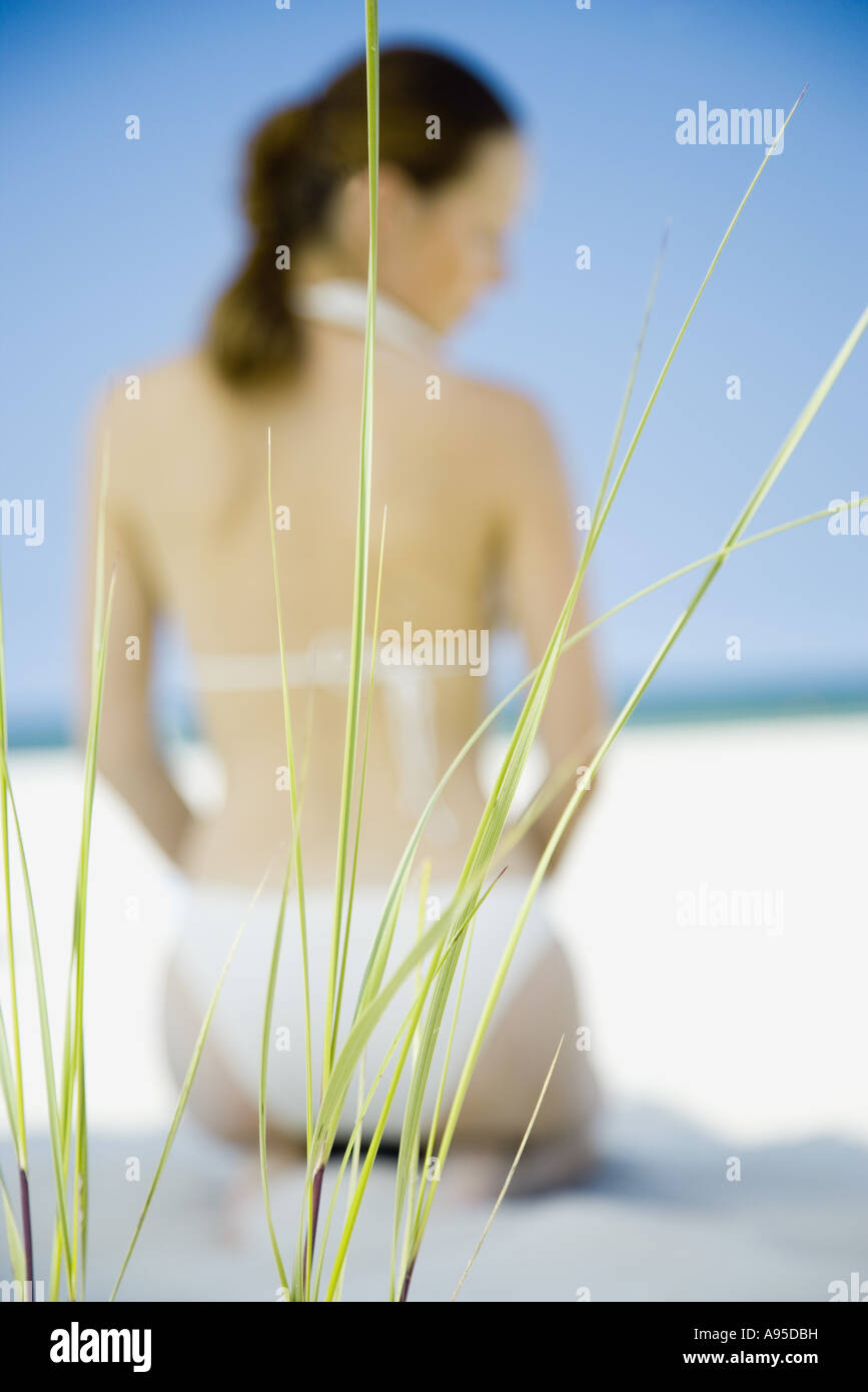 Woman in bikini kneeling on beach, focus on sea oats in foreground Stock Photo