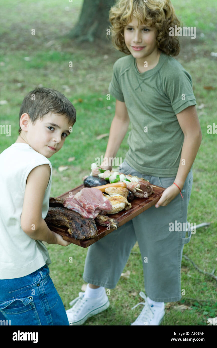Two boys carrying tray of grilled and raw meats Stock Photo