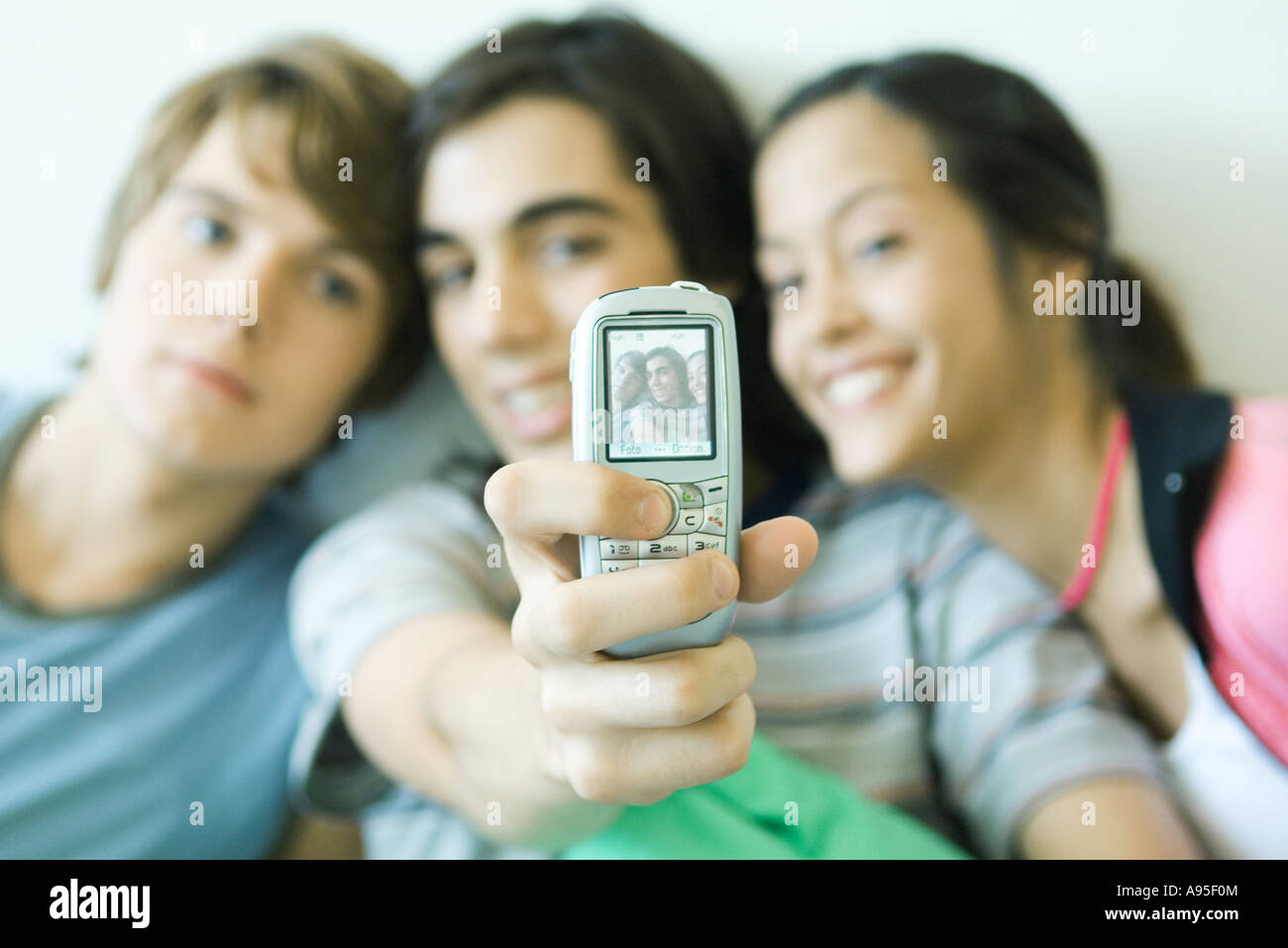 Teenage friends taking photo with cell phone, focus on phone in foreground Stock Photo