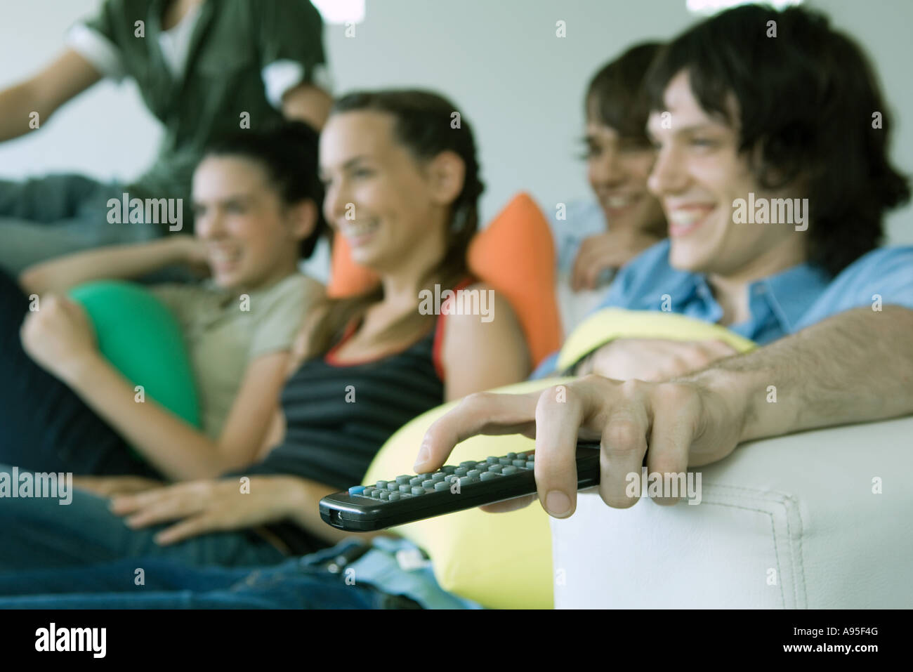 Teenage friends watching TV together, focus on remote control in foreground Stock Photo