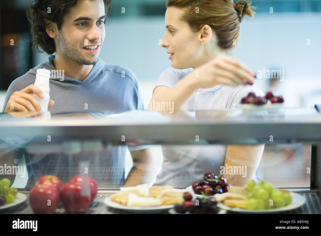 Two young adults standing at snackbar, chatting Stock Photo