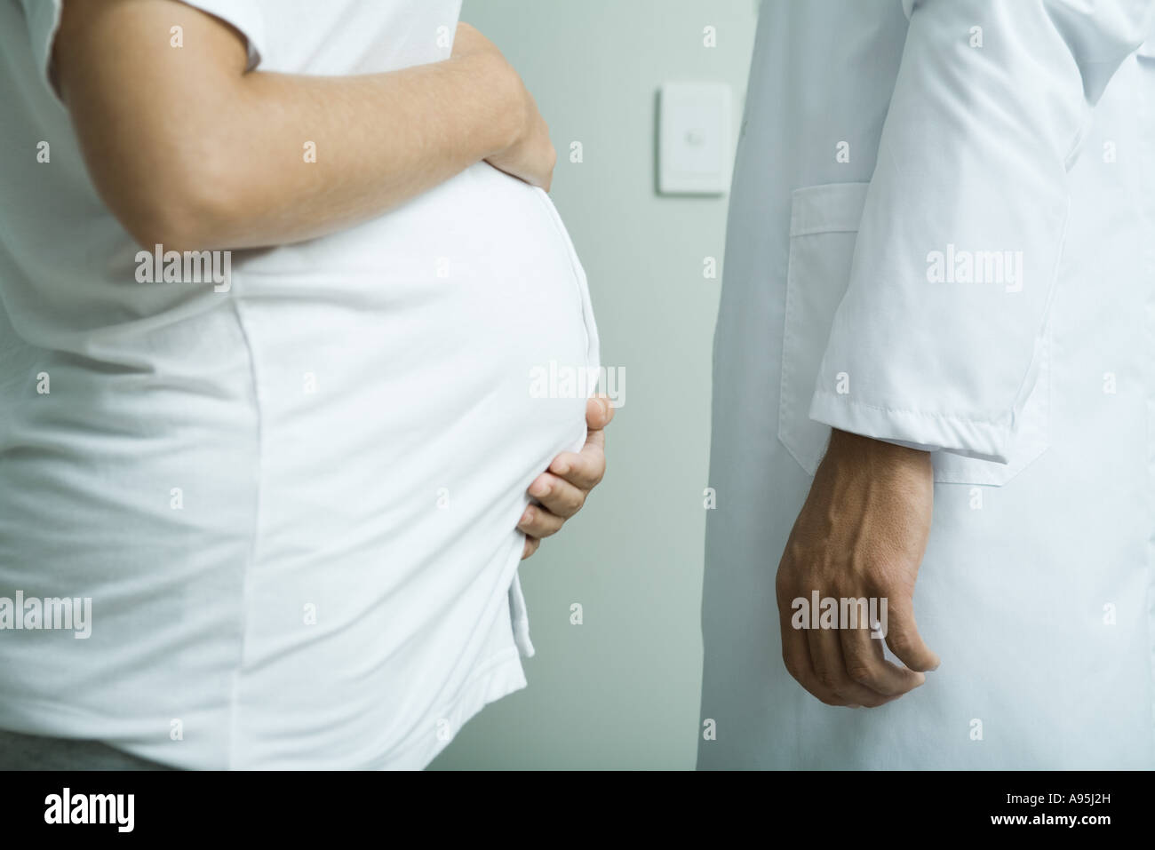 Pregnant woman standing face to face with doctor, mid section, side view Stock Photo