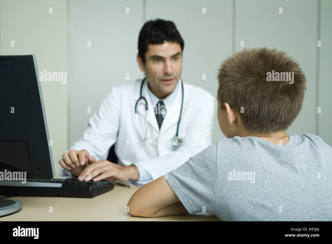 Doctor sitting across from boy, using computer Stock Photo