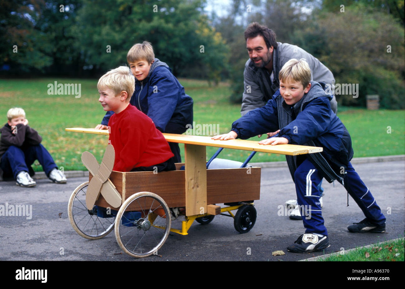 A father plays with his sons and their home made cart in the park. Stock Photo