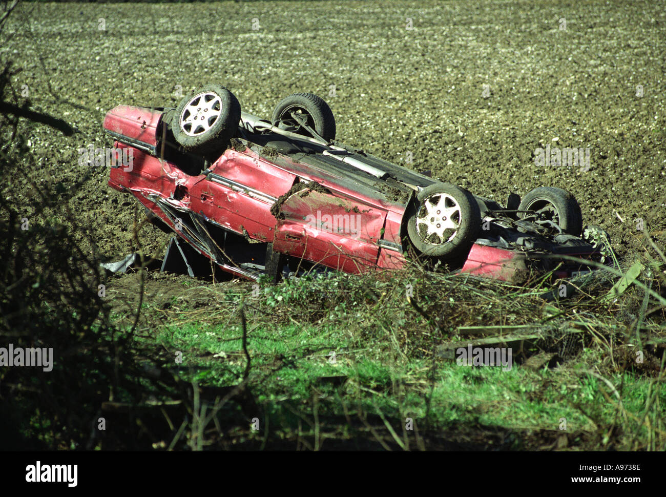 A crashed and overturned red car in a field Stock Photo