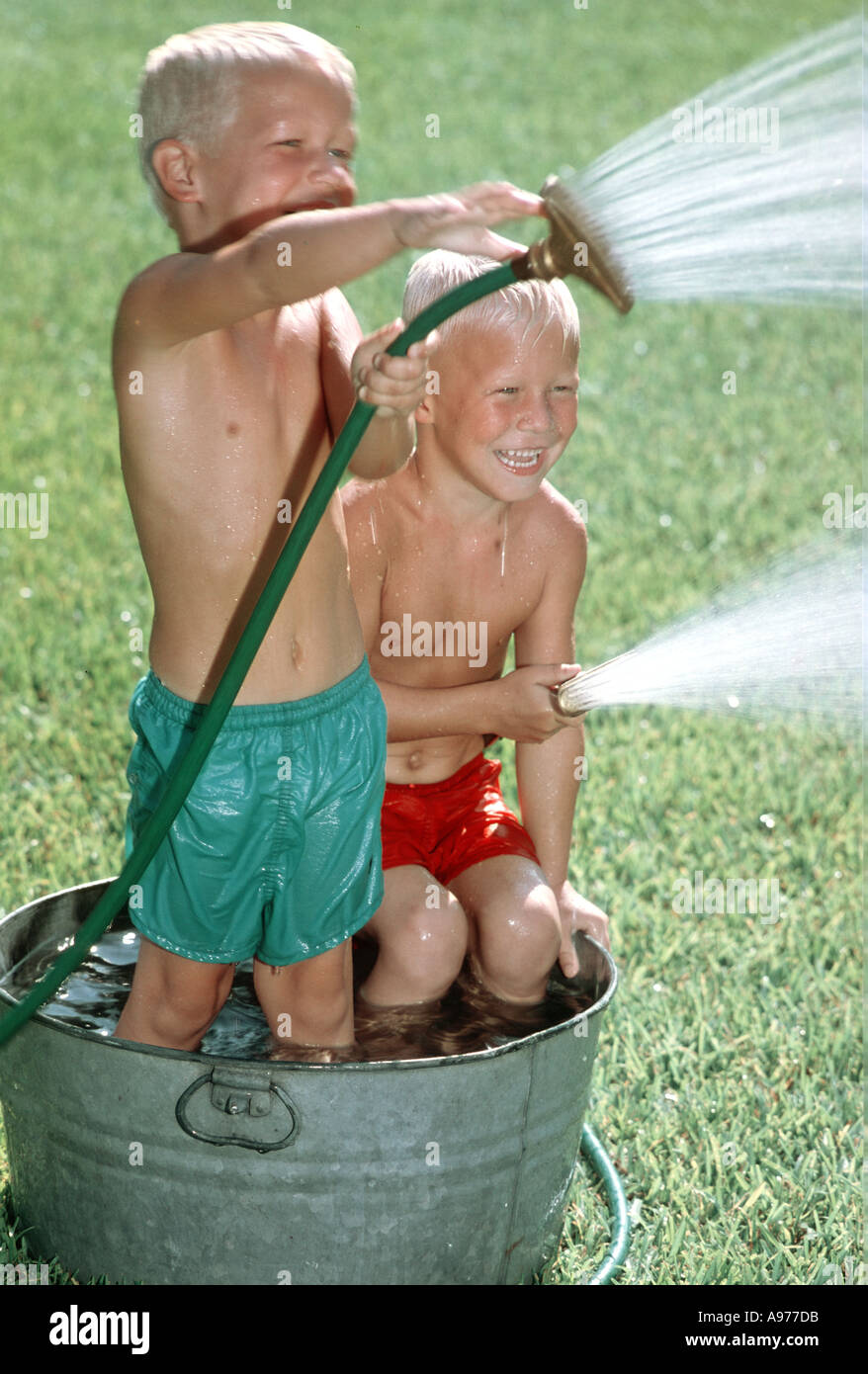 two boys in wash tub squirting water hoses Stock Photo