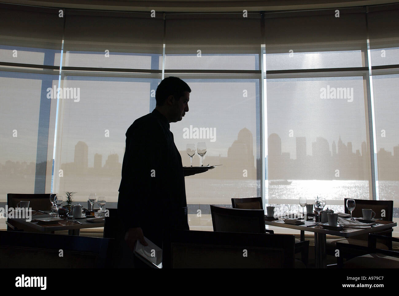 A waiter in silhouette passes a bank of windows in a hotel on the Hudson river Stock Photo