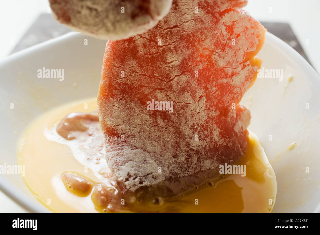 Breading veal escalope dipping meat in egg FoodCollection Stock Photo