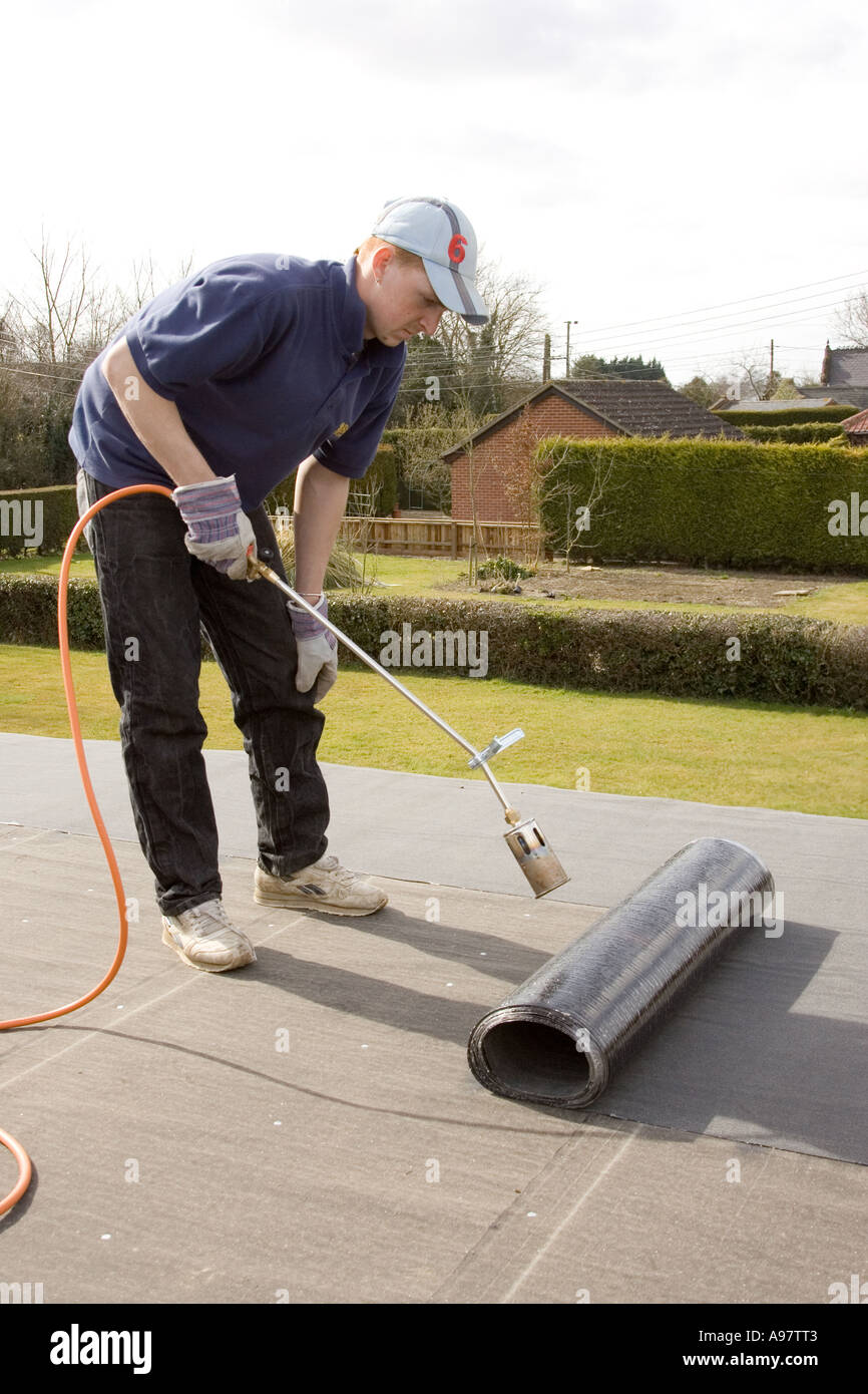 a builder using a gas blowtorch to heat and melt bituminous felt