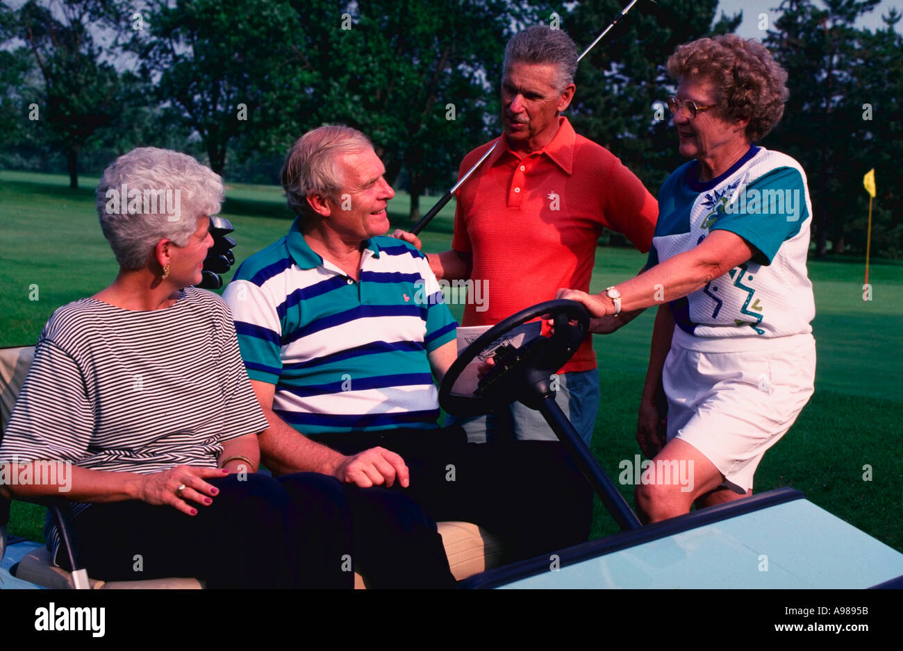 Two senior couples talking around a golf cart while playing golf Stock Photo