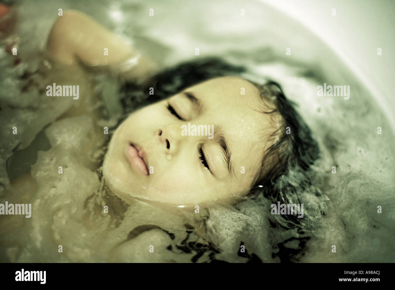 Girl aged 3 years with eyes closed lies back to rinse hair in bath