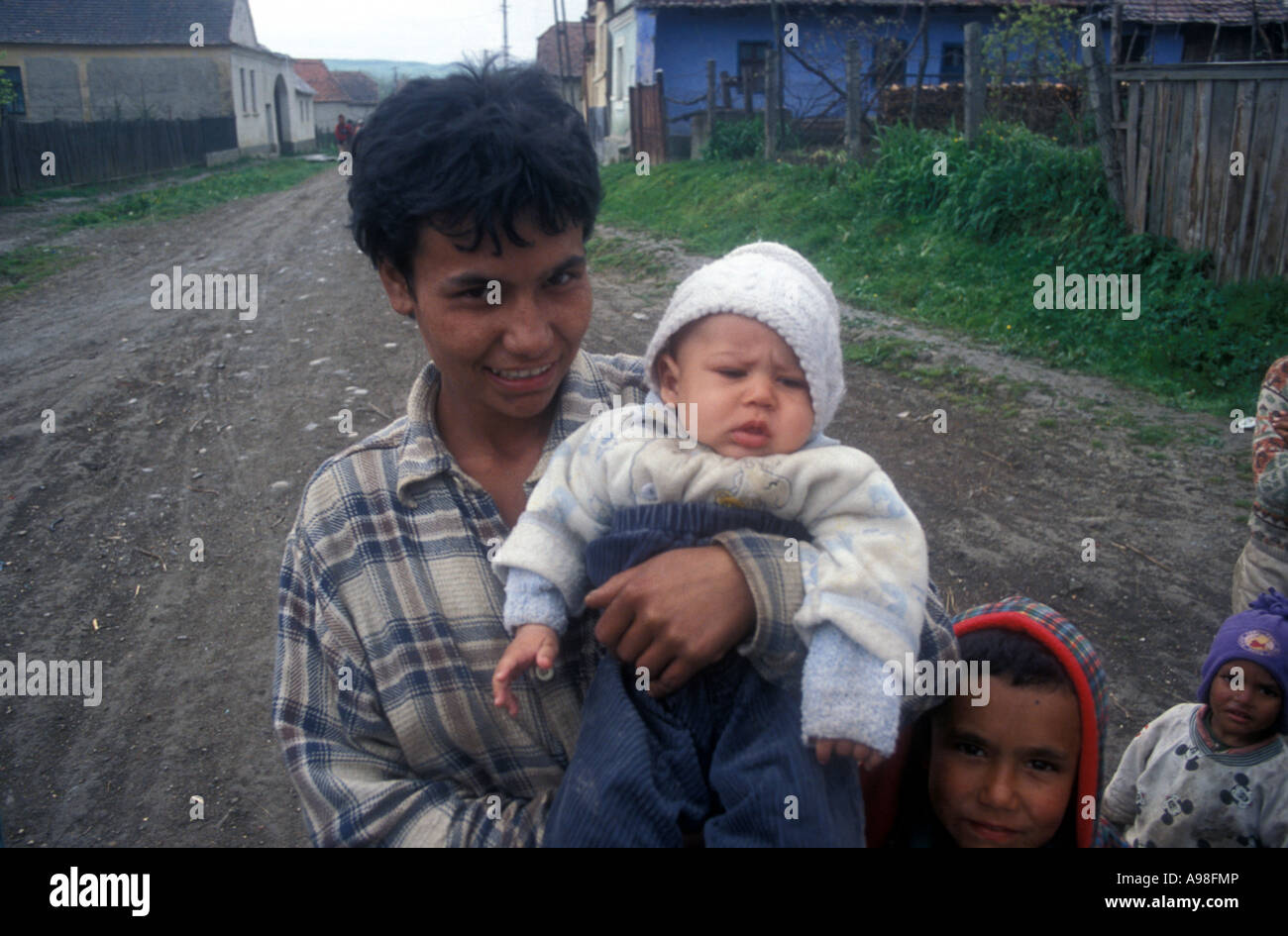 A Gypsy mother poses with a child as other children look on in Soard, Romania.  Note dirt street and small houses in background. Stock Photo