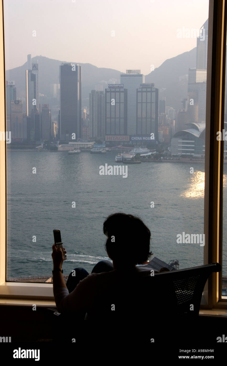 A woman using a mobile phone while overlooking Hong Kong harbour and ...
