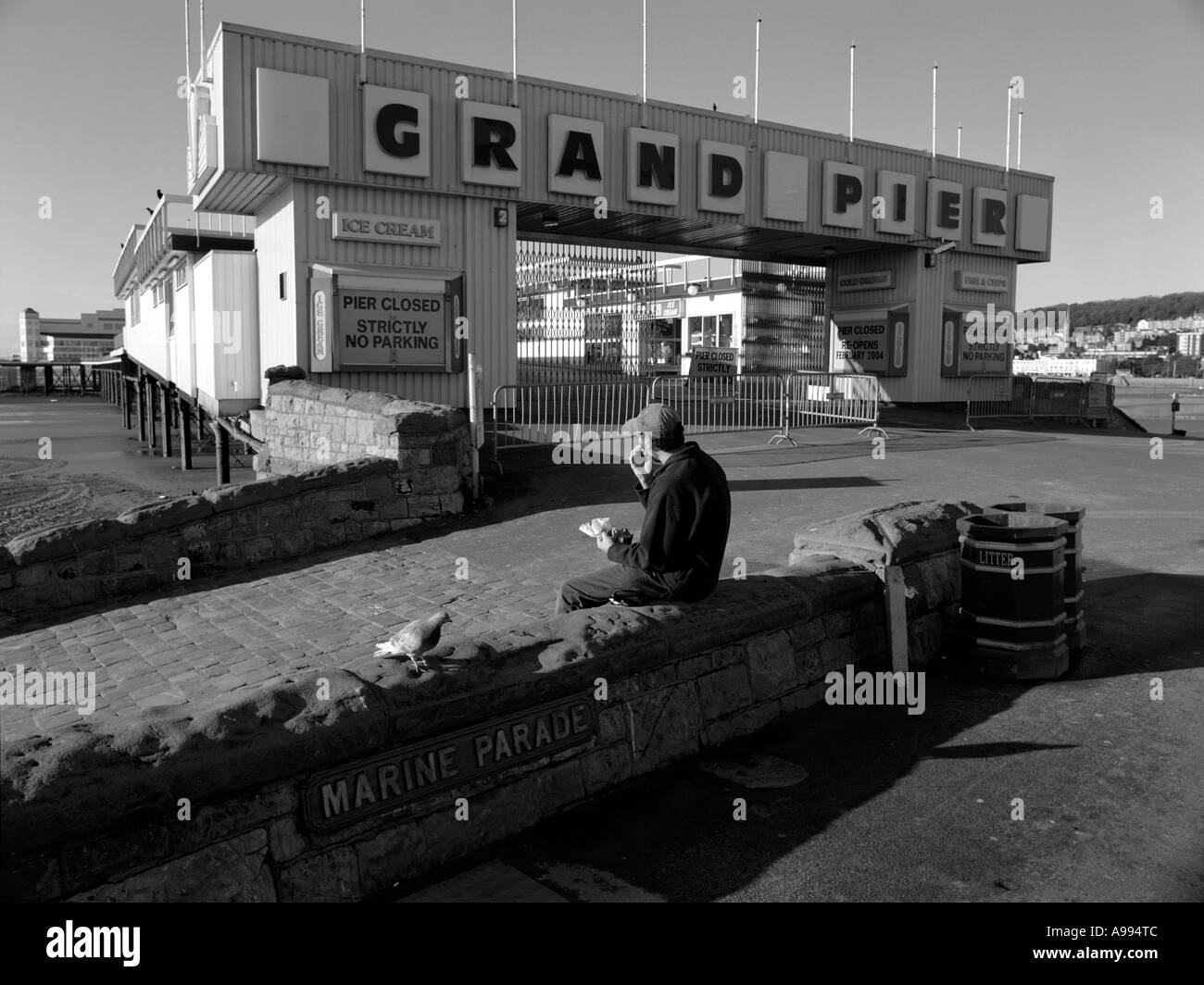 Young man eating his lunch on a wall outside the Grand Pier, Weston-Super-Mare, Somerset, England. (Black and White image) Stock Photo