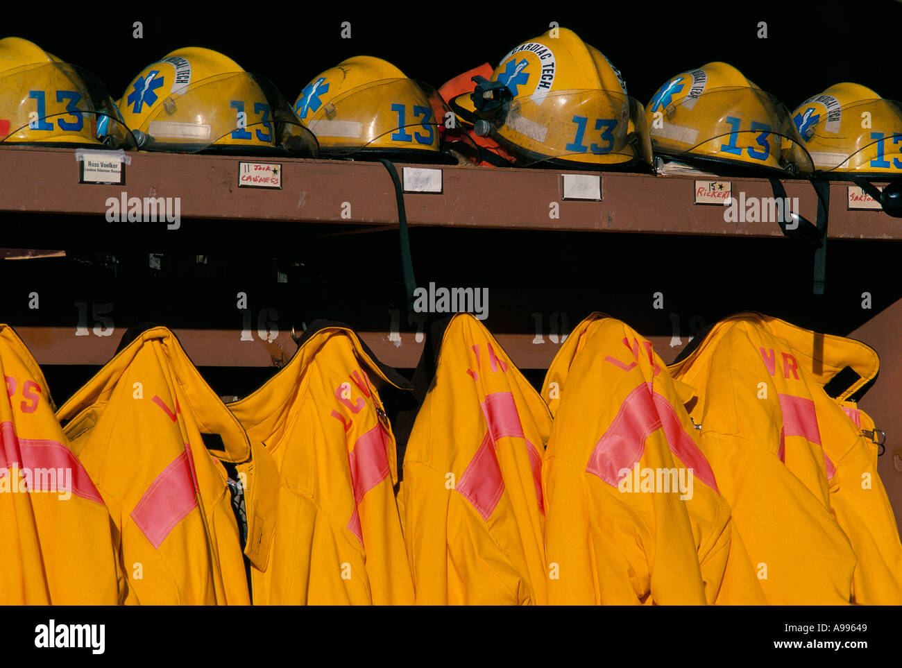 Bright yellow firefighter turnout gear coats and helmets stored on a ready rack organized for instant use Stock Photo