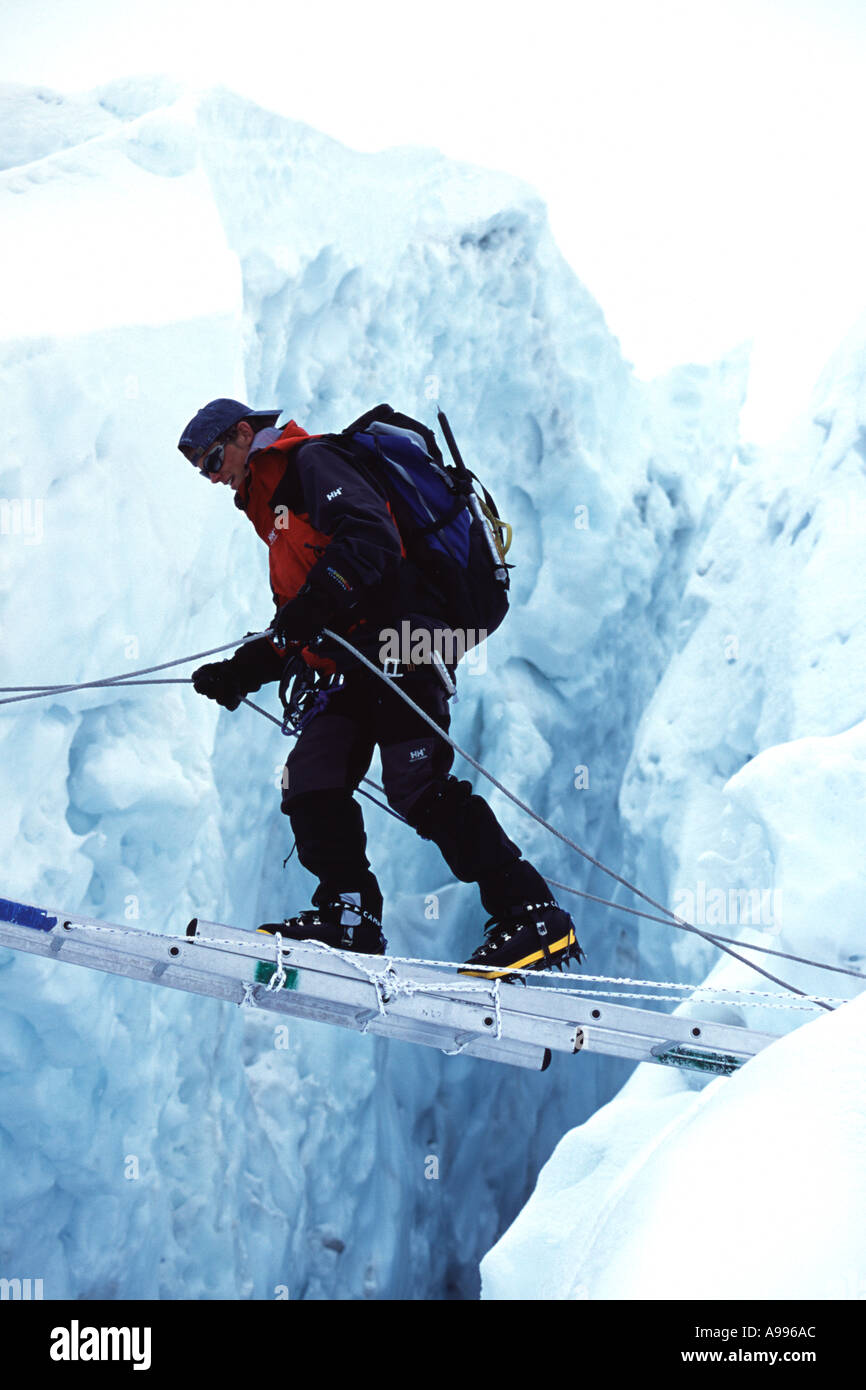 Burdened mountain climber uses a horizontally lying ladder to cross over a crevasse in the Khumbu Icefall region of Mt Everest Stock Photo