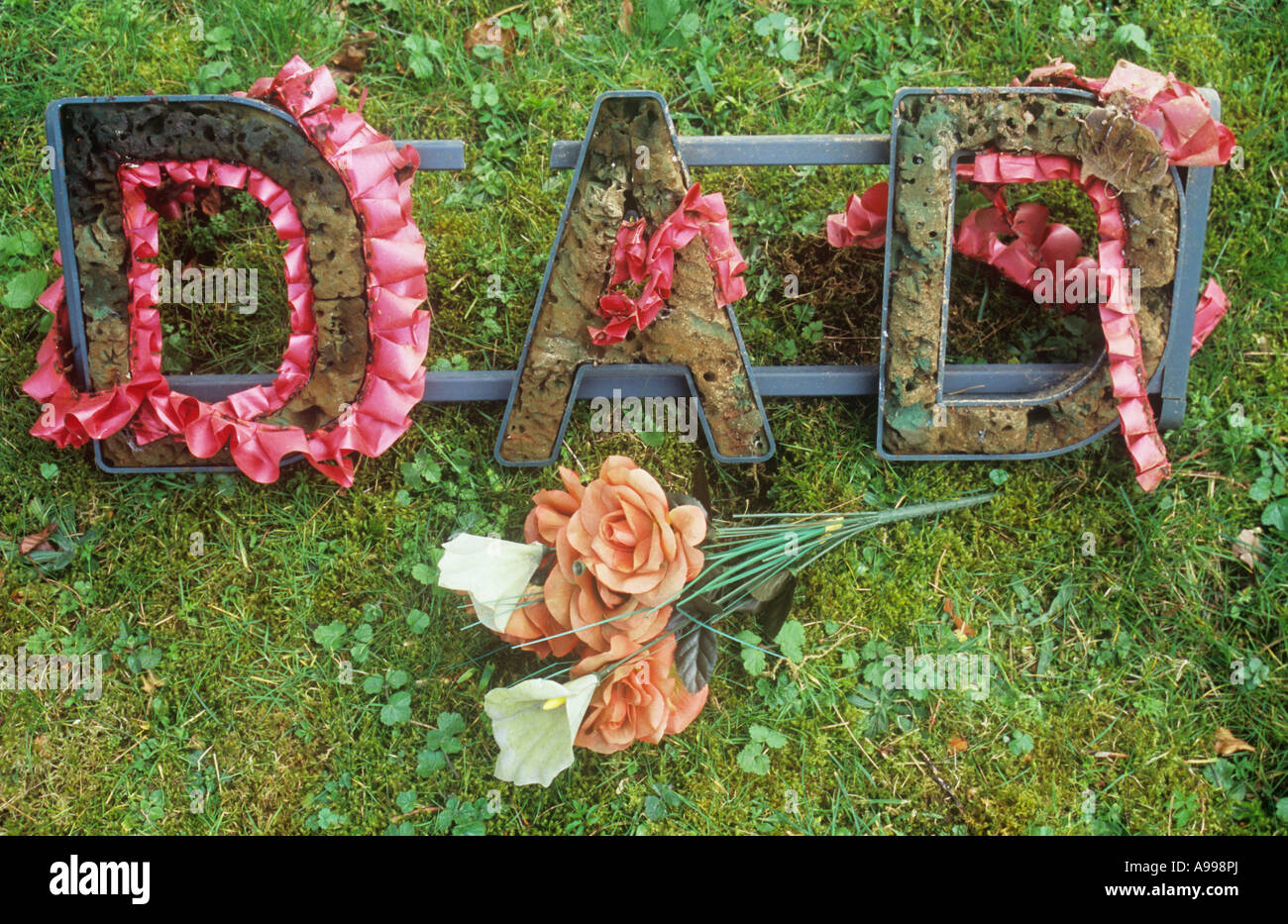 Plastic frame used to hold flowers and placed on coffins or graves stating DAD but now breaking with decorations lying on grass Stock Photo