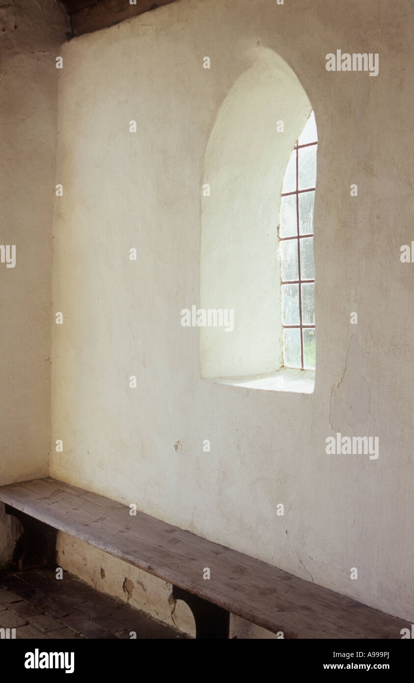 Interior view of small room or lobby or porch or hall with plain walls square leaded arched window and simple wooden bench Stock Photo