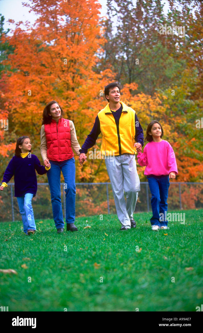 Hispanic couple and their two daughters holding hands and walking through the park Stock Photo