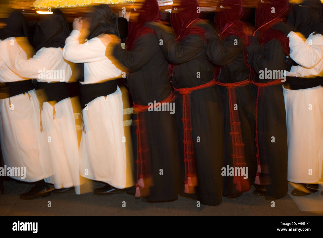Hooded members of a religious fraternity wearing robes carry a float ...