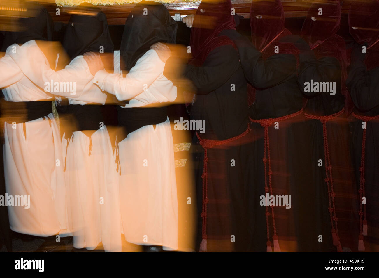 Hooded members of a religious fraternity wearing robes carry a float ...