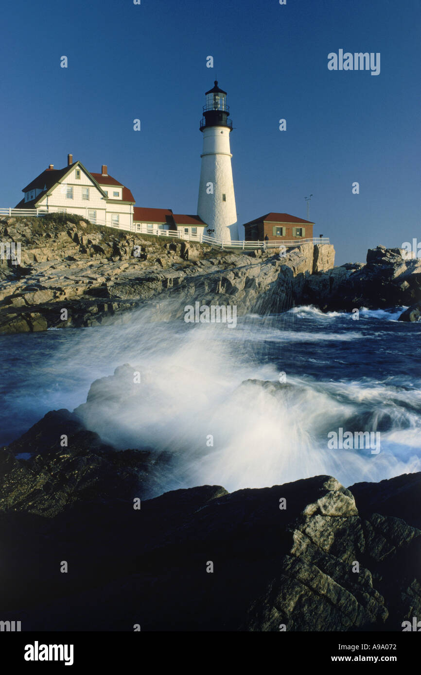 Portland Head Lighthouse in Maine at sunrise with waves crashing over rocky shore below Stock Photo