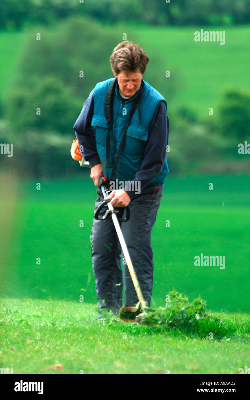 A man strimming weeds in a paddock using a Petrol driven strimmer Stock Photo
