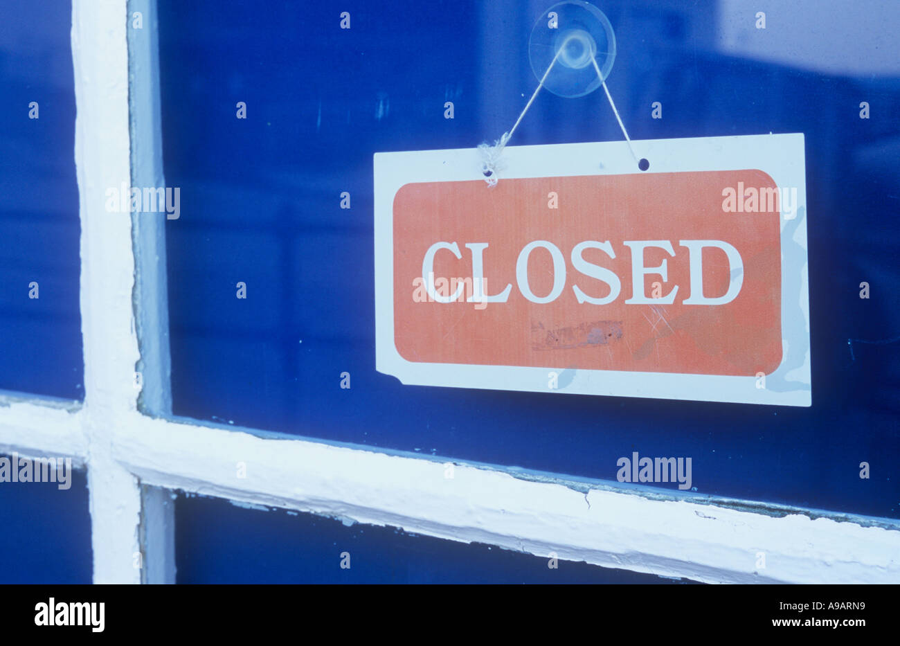 Close up of a red and white sign in a shop or kiosk or cafe window with blue blinds or curtains stating Closed Stock Photo
