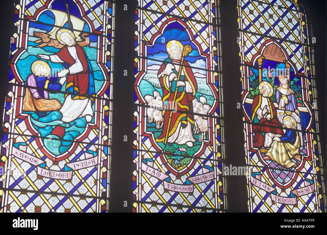 View of Victorian stained glass church windows with scenes of Jesus on the water and as a shepherd and with Mary Magdalene Stock Photo