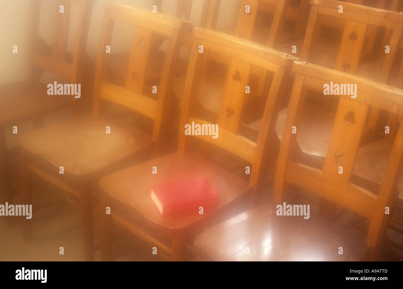 Atmospheric rows of simple wooden chairs with a red book lying on a seat bathed in golden sunlight Stock Photo