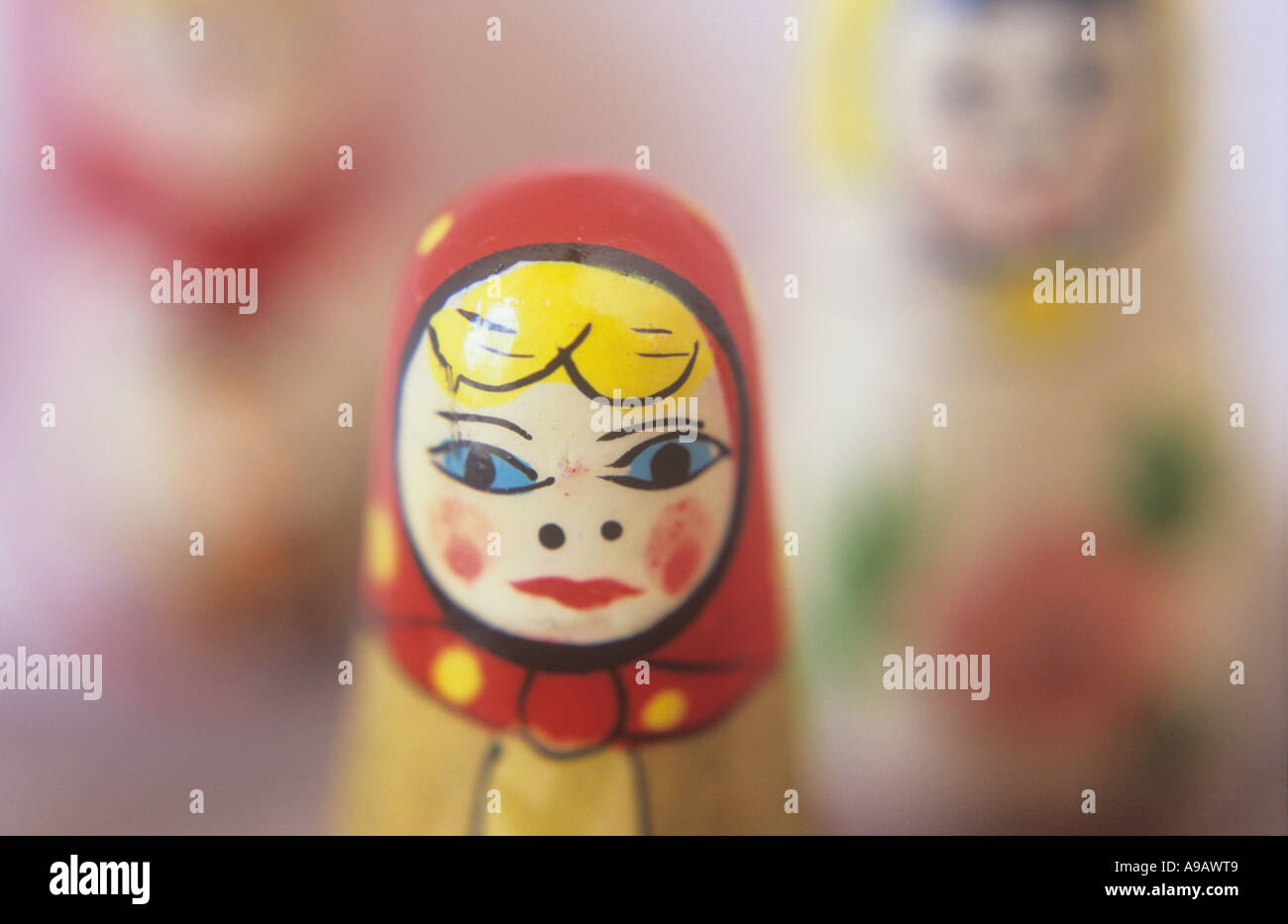 Close up of the face and headscarf of a painted wooden Russian doll with two others in the distance behind her Stock Photo