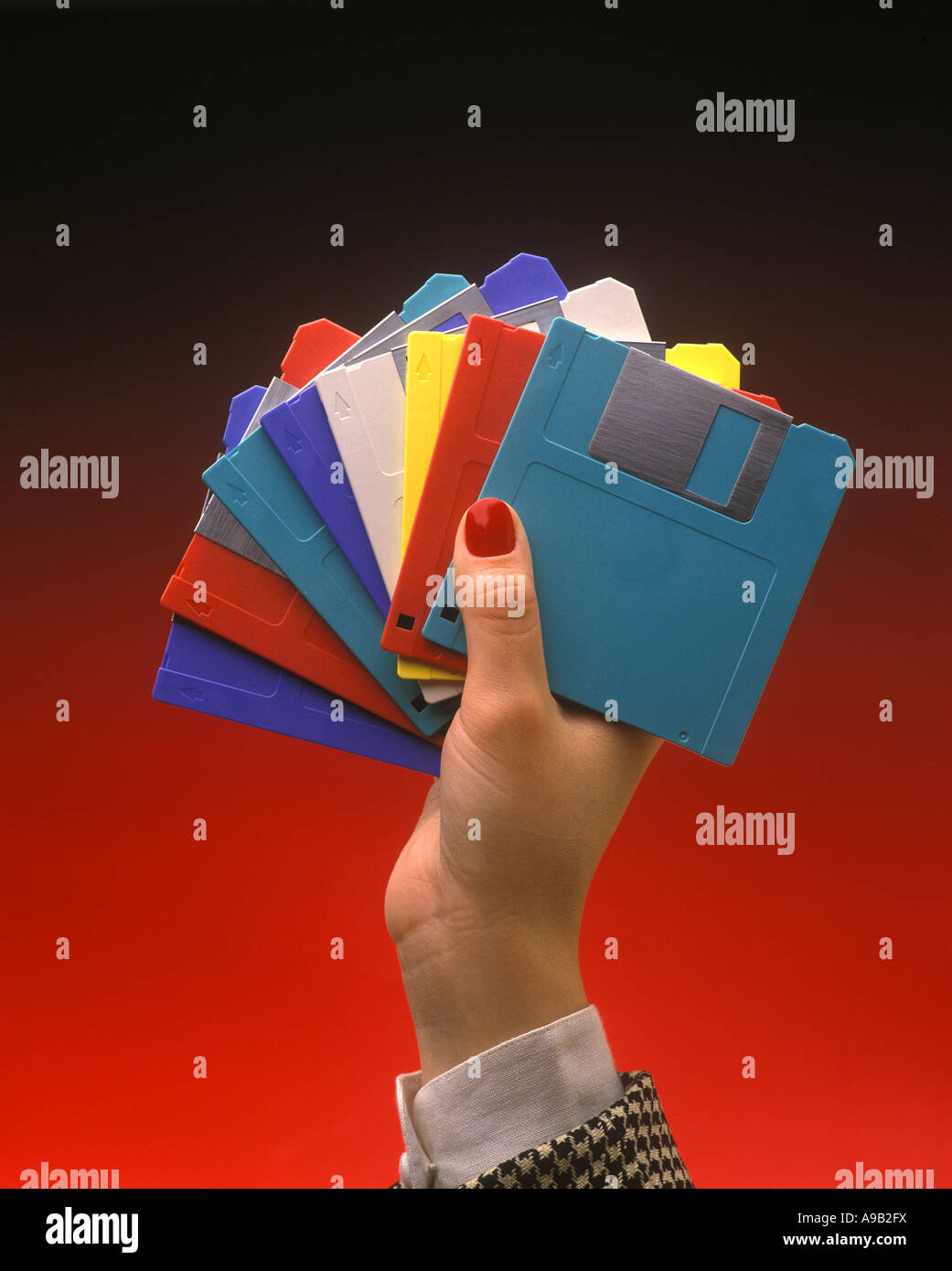 1991 HISTORICAL WOMAN’S HAND HOLDING MULTICOLORED 3.5 INCH MULTICOLORED MICRO FLOPPY DISCS (©IBM CORP 1973) ON PLAIN RED BACKGROUND Stock Photo