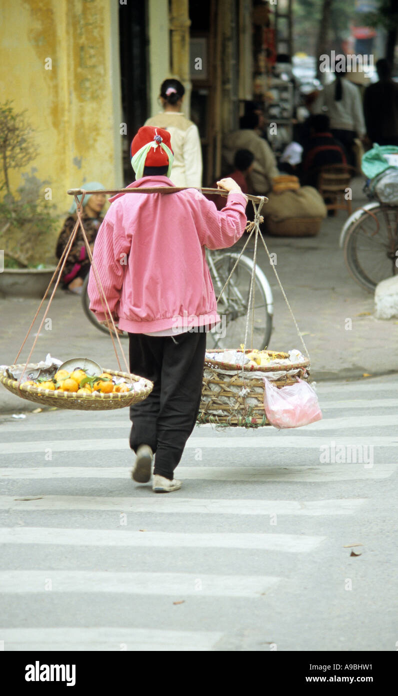 Woman carrying fruit baskets crossing Nha Tho St, Hanoi Old Quarter, Viet Nam Stock Photo