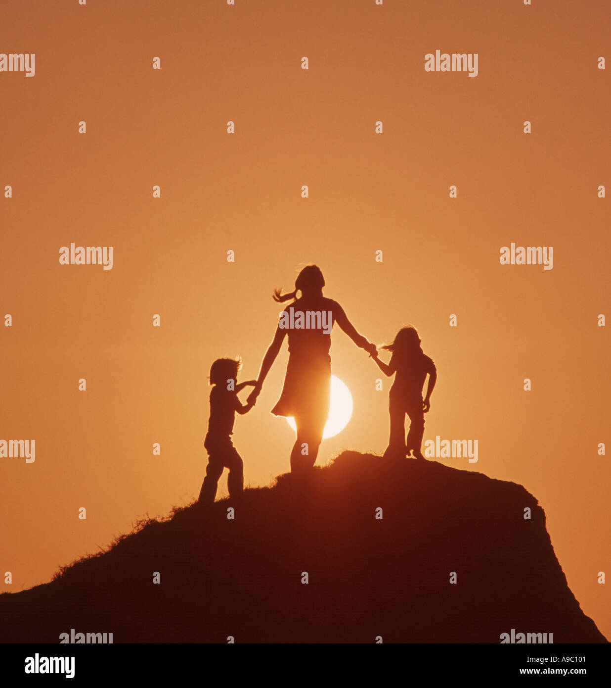 mother and two children standing atop a hill at sunset Stock Photo