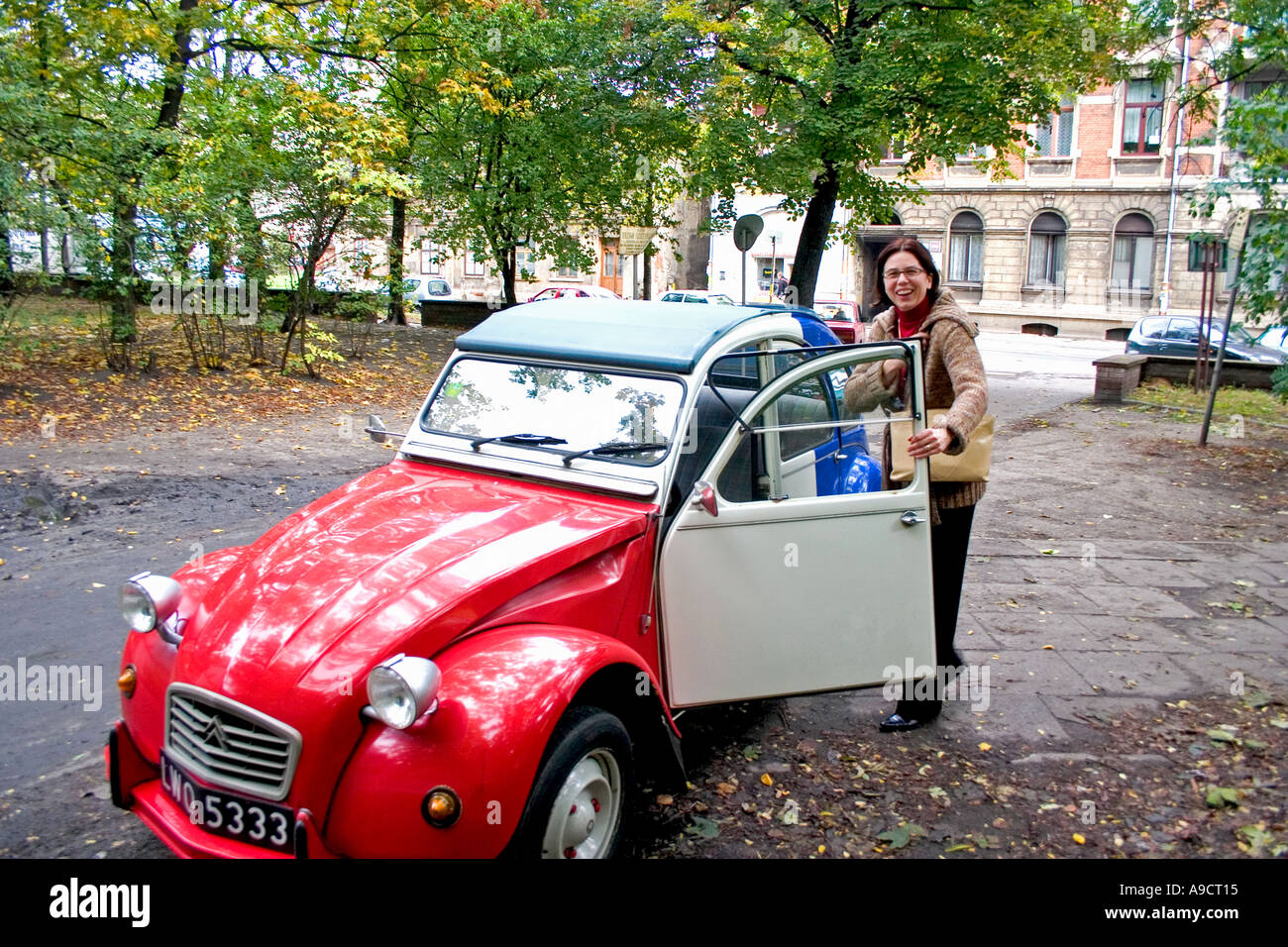 Owner stepping into beautiful red white and blue Citroen 2CV or French Deux Chevaux auto in courtyard. Lodz Poland Stock Photo