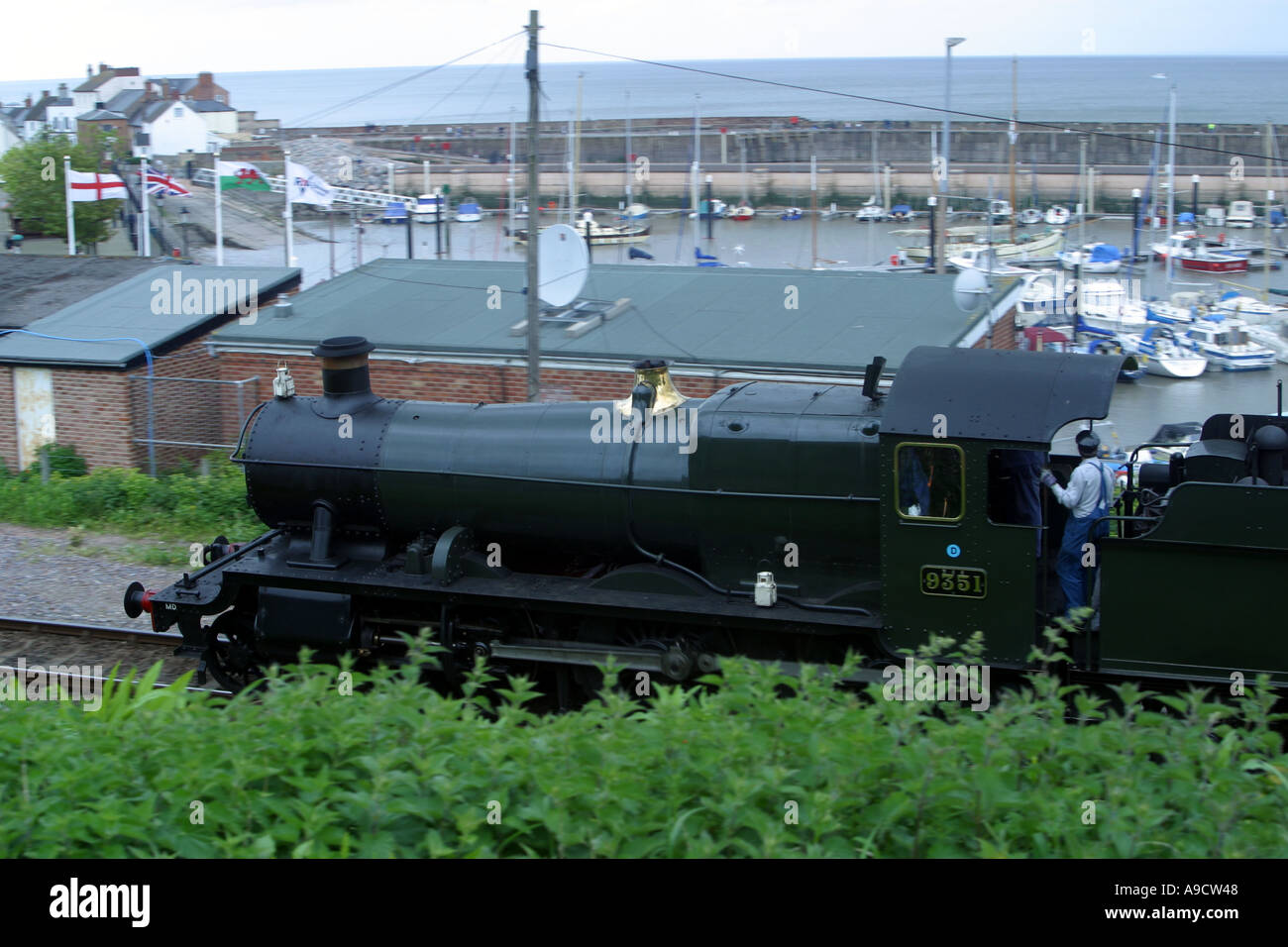 STEAM TRAIN APPROACHING WATCHET STATION WITH HARBOUR IN BACKGROUND SOMERSET ENGLAND Stock Photo