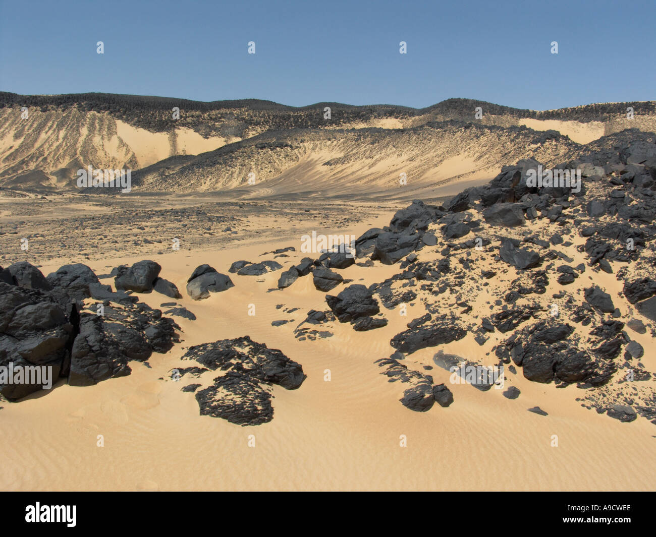 Shiny black volcanic rock strewn over the sand in the Black Desert Western Egypt Stock Photo