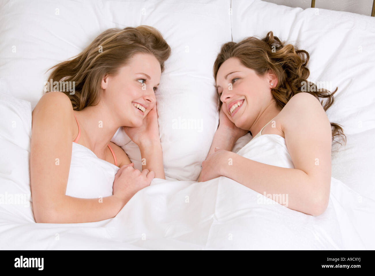 two young women lying in bed smiling at each other Stock Photo - Alamy