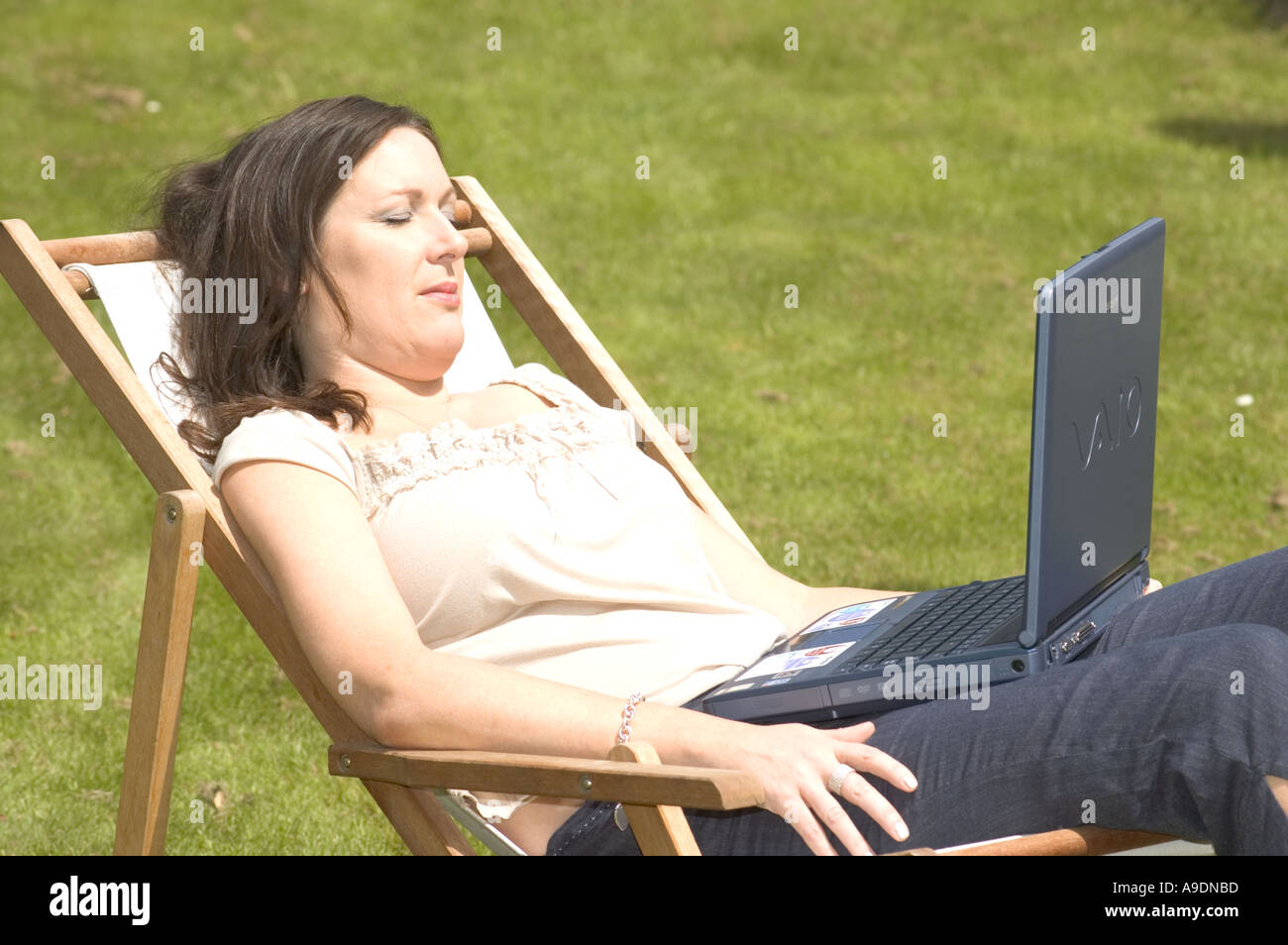 Young woman sitting on a deck chair in the garden or a park using a ...