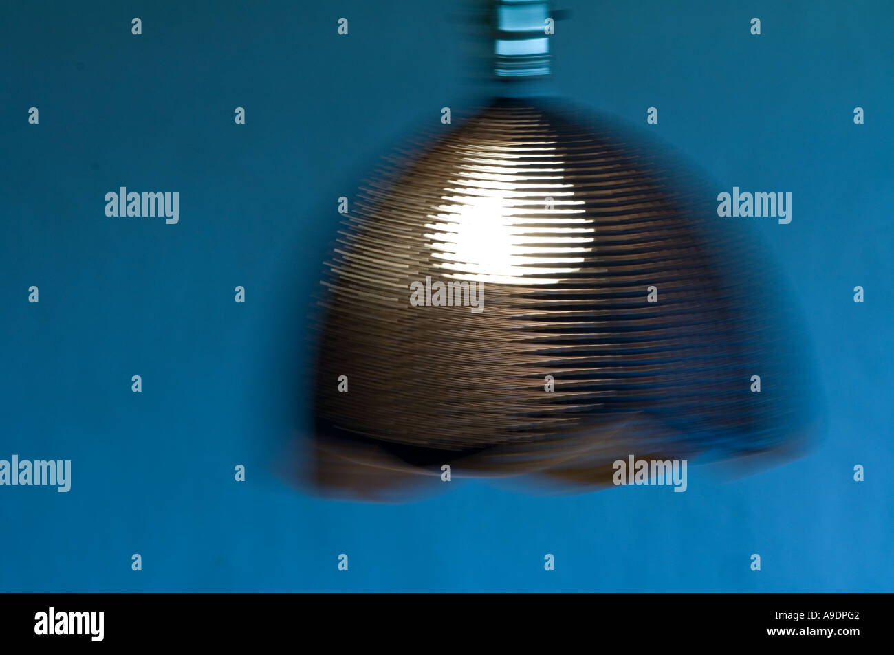 swinging illuminated lamp hanging from ceiling with perforated lamp shade Stock Photo