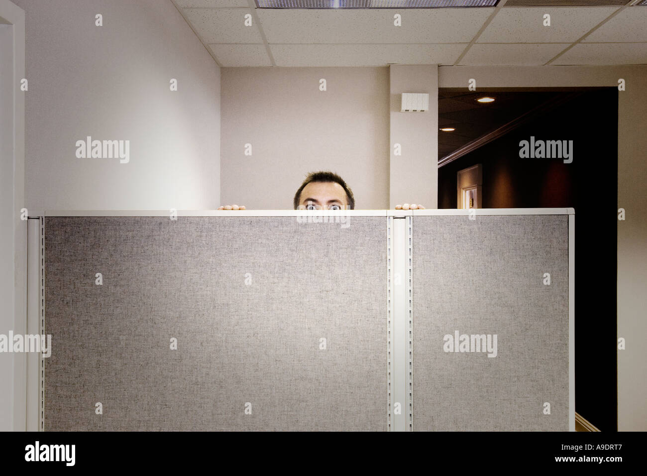 grainy shot of frightening man peeking over cubicle wall Stock Photo