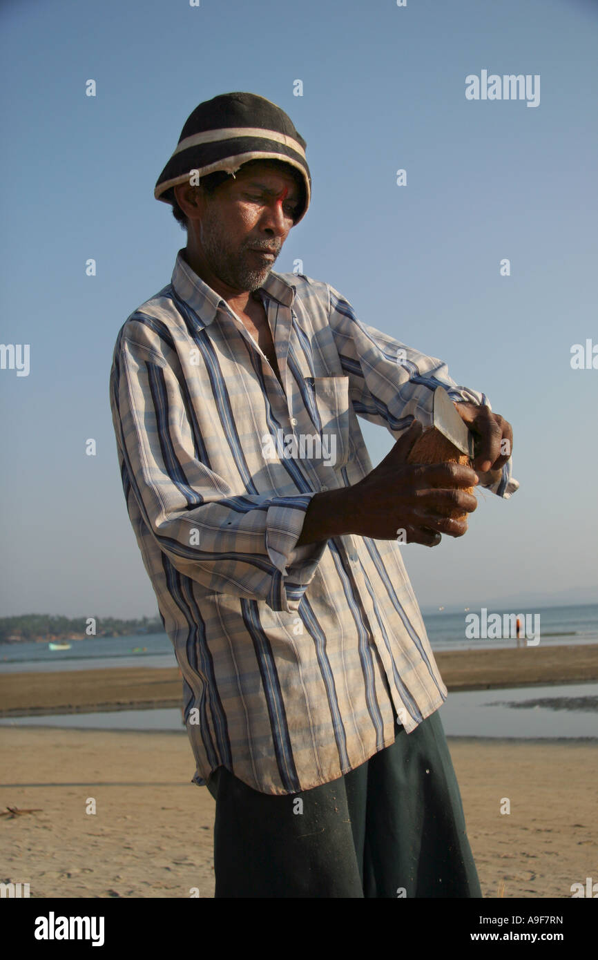 A street vendor prepares a coconut for sale to a tourist on the beach