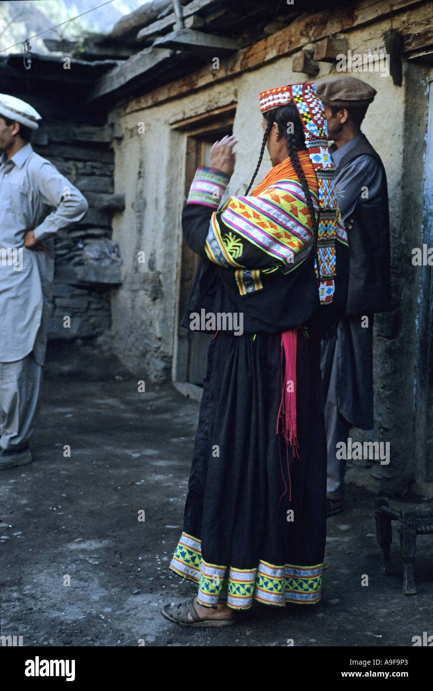 Kalash woman in traditional dress with two local men behind Bumboret village Kalash valley North West Frontier region Pakistan Stock Photo