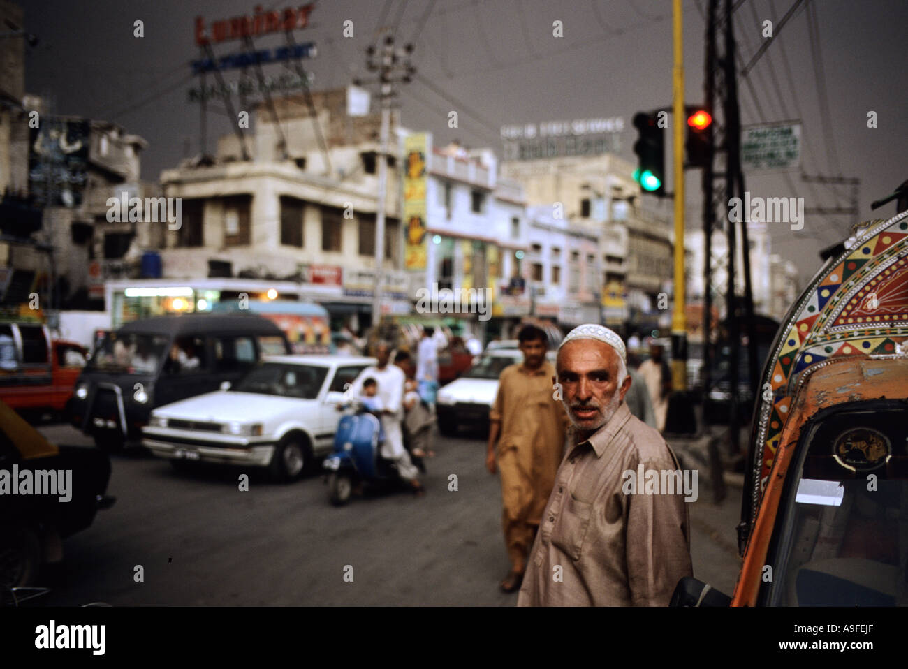 Old man in traditional clothes stands alone in busy street in