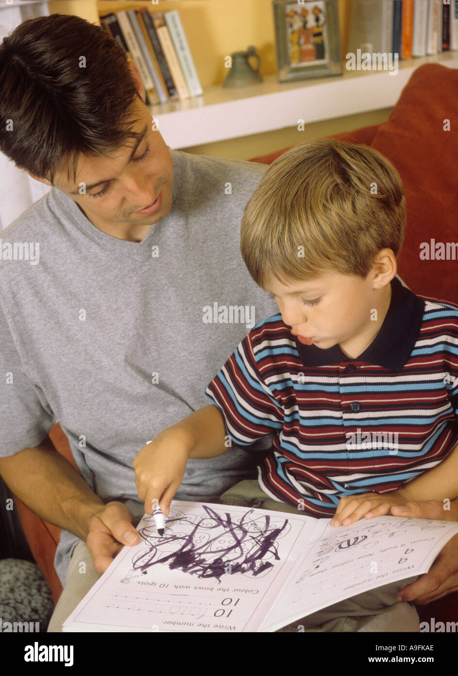Father watching his young son play with a colouring book Stock Photo