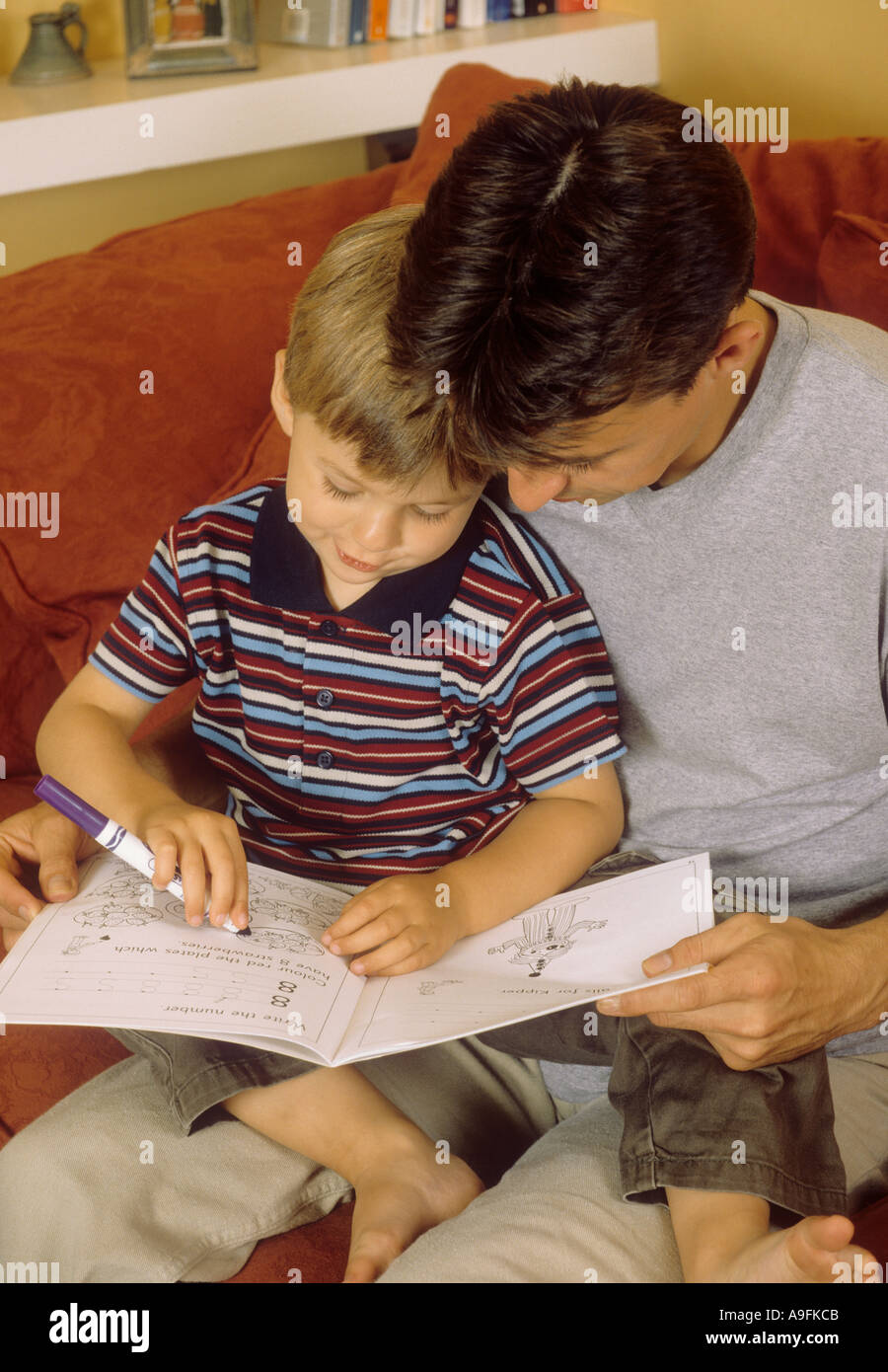 Father watching his young son play with a colouring book Stock Photo