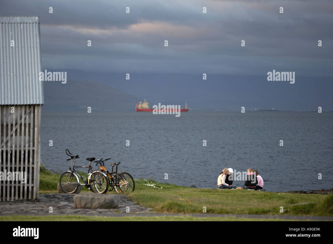 Young teenagers sitting and talking and a big ship sailing to Reykjavik harbour in the back Stock Photo